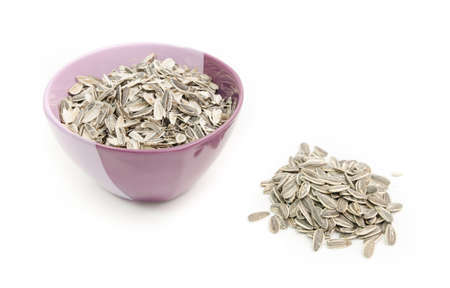 Sunflower seeds and husks in a bowl on a white isolated background with the peel in th bowlの写真素材