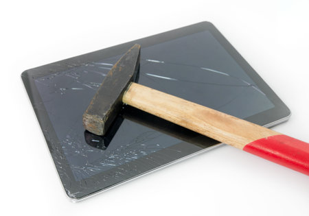 Hammer on a tablet with a cracked broken touchscreen glass suggesting the need for repair and service under warrantyの写真素材