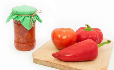 Traditional romanian vegetable preserve called zacusca in a jar with fresh vegetables on a wood board on a white isolated background and a green jar lidの写真素材