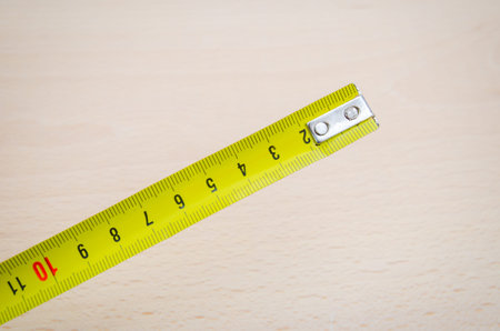 Yellow measruing tape with a yellow look an a wood board