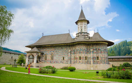 SUCEVITA, ROMANIA - 8 AUGUST 2014: SUCEVITA orthodox Monastery in Moldavia Region of Romania famous for it's painted religios scenes onn the wall on a sunny summer day with a blue cloudy sky and a green gardenのeditorial素材