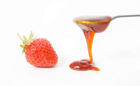 Strawberry jam suggested by a spoon filled with red sauce and dripping or pouring on the white background with a close berry in the viewの写真素材