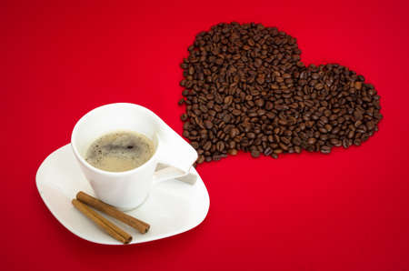 Romantic coffee cup for valentine's or any other couple celebration on a inspiring red background with a heart made fdrom coffee beansの写真素材