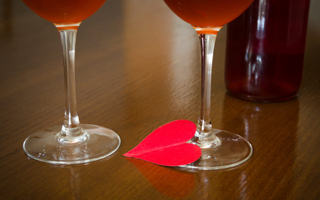 Love and romance suggested by a red heart two wine glasses and a bottle of rose wine on the background in a dimm romantic lightの写真素材