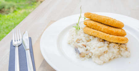 Soya schnitzel with rice and mushrooms on a white plate and a wooden table at a restaurant outdoor terrace on a sunny spring dayの写真素材