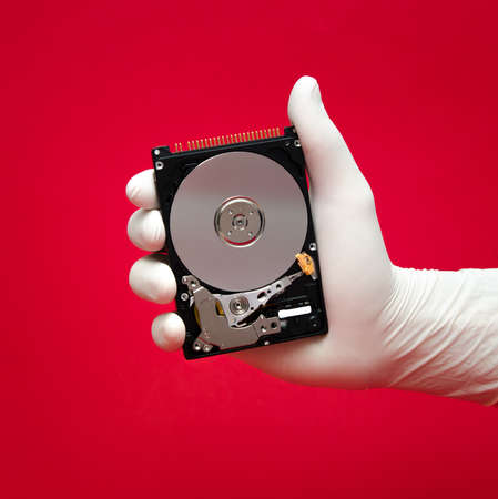 A hard disk being held by a scientist or repairman's hand on a red with valuable files awaiting to be recoveredの写真素材
