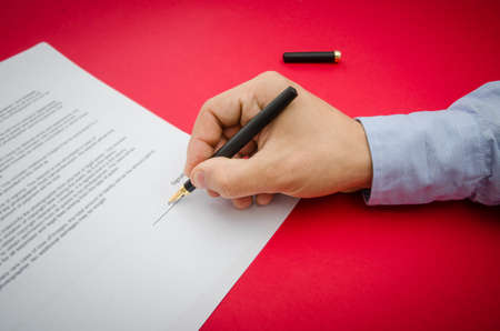 Sign here suggested by signing the document or contract by a business man hand on a red alerted backgroundの写真素材