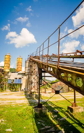 Old abandoned forgotten industrial site with a close view of a conveierbelt with steel beams and two towers on the background on a sunny summer day with blue cloudsの写真素材