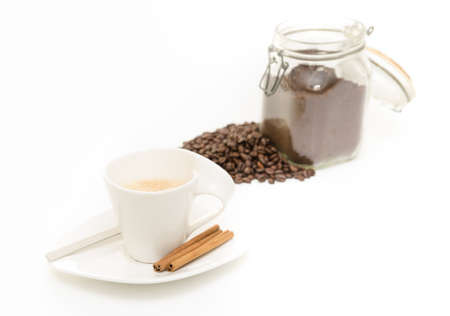 Coffe cup with fresh brewed cappucino on white plate with cinamon  a spoon and grind coffee and beans on the backgroundの写真素材