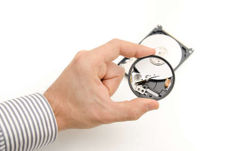 A tech guy inspecting a hard disk through a magnifying glass looking for broken pieces in order to recover files and dataの写真素材