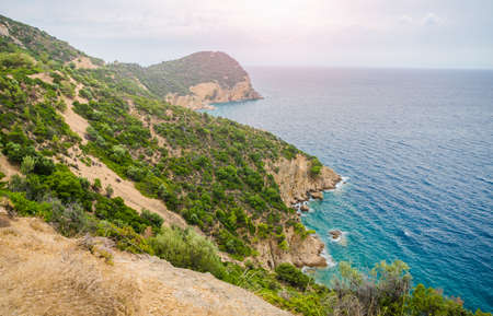 Epic view of greek coast from above with a blue turquoise water green bushes on cliffs and a beautiful sun on the horizon on a sunny summer day suited for a wallpaperの写真素材