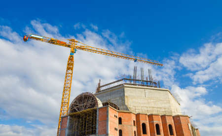 Constructing a tall impressive monument with a high yellow crane on a sunny summer day with a blue skyの写真素材