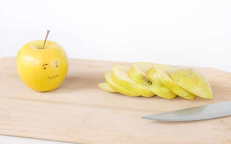 A scared sad apple looking at his chopped up friend on a wood board sliced with a knifeの写真素材