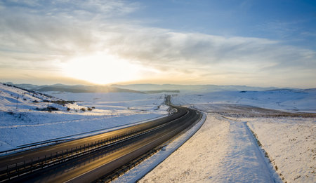 Empty and silent highway road over the mountains at sunset on a sunny winter day with snow transmitting freedom power and hopeの写真素材