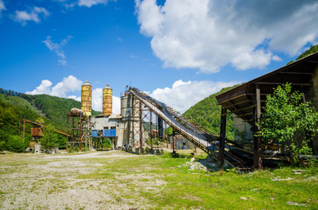 Old abandoned industrial concrete factory with unused towers on a sunny summer day with green...