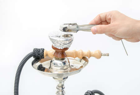Putting a piece of coal on a hookah or shisha to start smoking the aromatic plant mixture on an isolated backgroundの写真素材