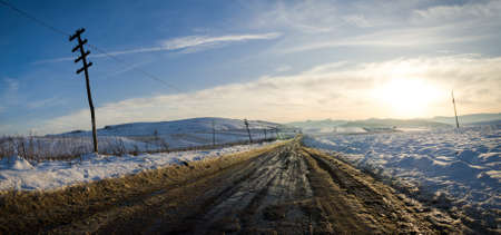 Rural unpaved road waving over the hills and mountains on a snowy winter day at a bright melancolic sunsetの写真素材