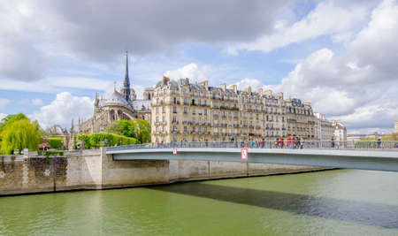 Paris, France: The Seine river in Paris with a bridge full of tourists and The Notre Dame de Paris gothic catholic Cathedral and other french buildings on a sunny spring dayの写真素材