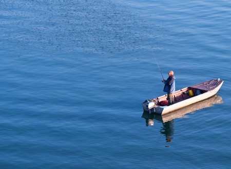 Fisherman standing on a boat and fishing in sea の写真素材