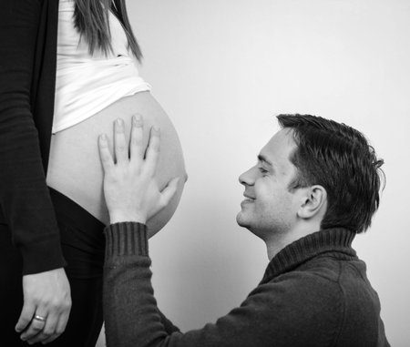 Close up of a man kissing the belly of his lovely pregnant wife in black and white