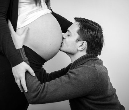 Close up of a man kissing the belly of his lovely pregnant wife in black and whiteの写真素材