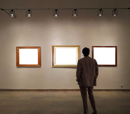 Man in gallery room looking at empty picture framesのeditorial素材