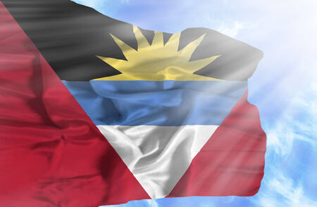 Antigua and Barbuda waving flag against blue sky with sunraysの写真素材