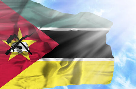 Mozambique waving flag against blue sky with sunraysの写真素材