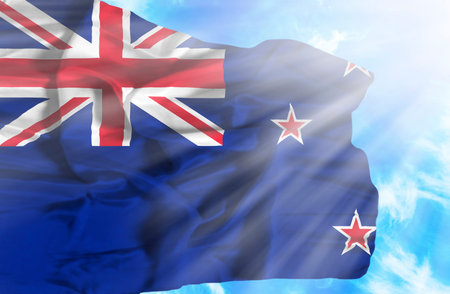 New Zealand waving flag against blue sky with sunraysの写真素材