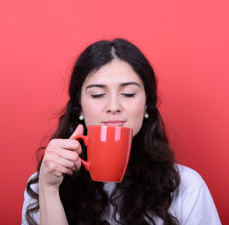 Portrait of happy woman enjoying cup of coffee against red backgroundの写真素材