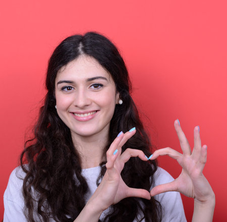 Portrait of happy woman making heart shape with hands against red background