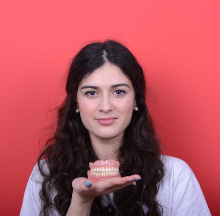 Portrait of happy woman with healthy smile holding denture against red background
