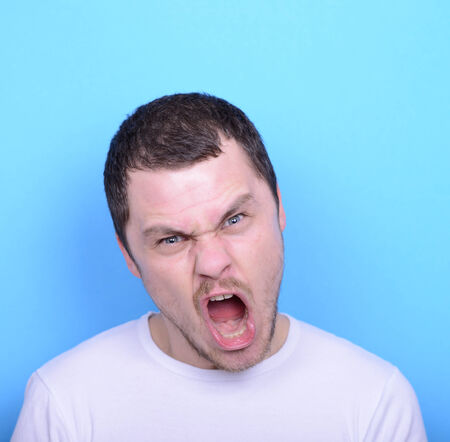 Portrait of angry man screaming and pulling hair against blue backgroundの写真素材