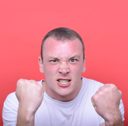Portrait of angry man screaming showing fist against red backgroundの写真素材