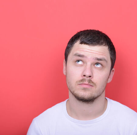 Portrait of man thinking and looking up against red backgroundの写真素材
