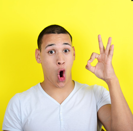 Portrait of funny man showing OK gesture with hands against yellow backgroundの写真素材