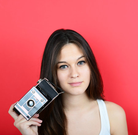 Portrait of young female holding vintage camera against red backgroundの写真素材