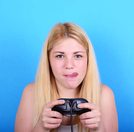 Portrait of girl holding game controller and playing games against blue backgroundの写真素材