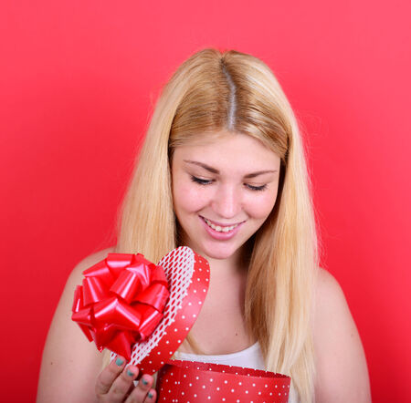 Portrait of happy woman opening gift box against red backgroundの写真素材