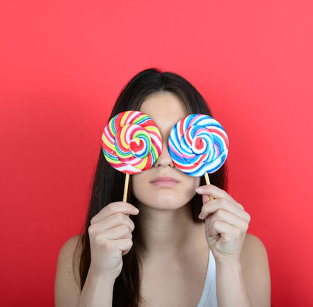 Portrait of woman covering eyes with lollipops against red backgroundの写真素材