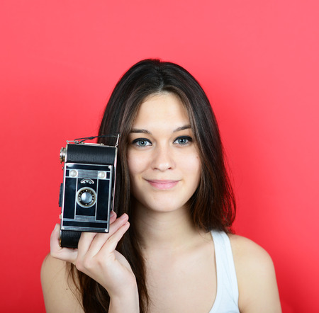 Portrait of young female holding vintage camera against red backgroundの写真素材