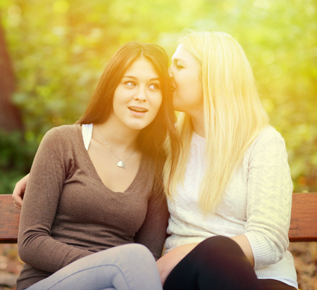 Two girl friends whispering secrets outdoorsの写真素材