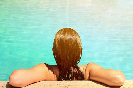Back view of relaxed woman in swimming pool with blue waterの写真素材