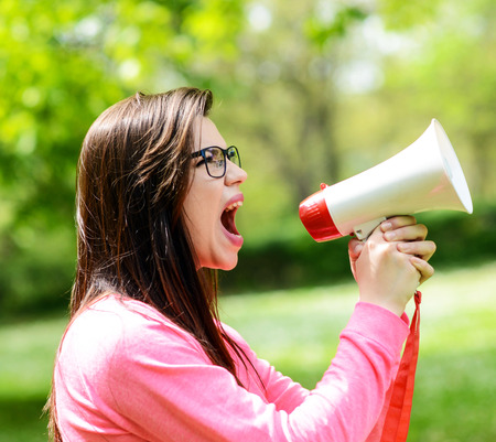 Portrait of middle aged woman shouting using megaphone against a nature backgroundの写真素材