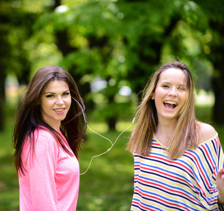 Female student girls outside in park listening to music on headphonesの写真素材
