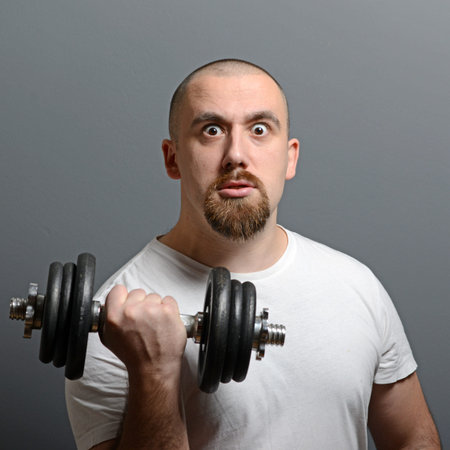 Portrait of a funny man holding dumbbells against gray background