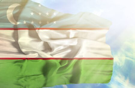 Uzbekistan waving flag against blue sky with sunraysの写真素材