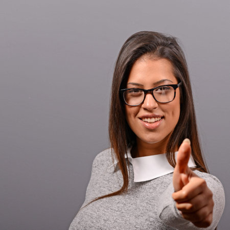 Portrait of happy woman holding thumbs up against gray background