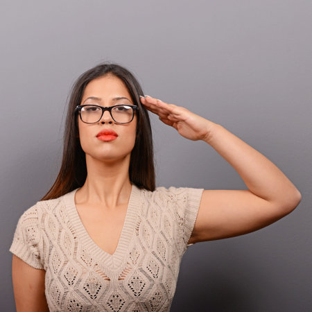 Portrait of serious woman saluting in casual clothes against gray background