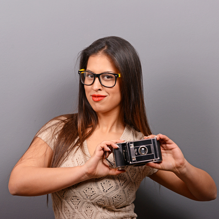 Portrait of a young woman holding retro camera against gray backgroundの写真素材